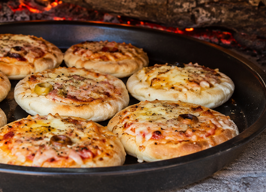 Detail malych kulatych mini pizz se zlatymi okraji a rozteklou mozzarellou